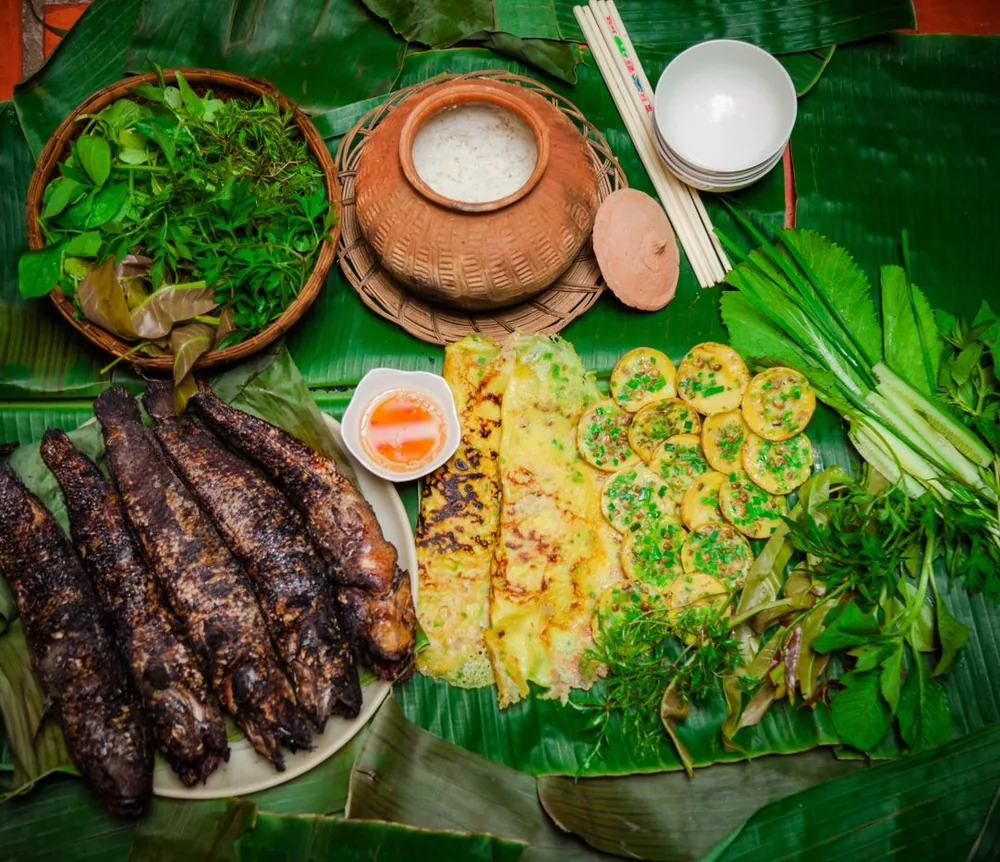 Cá nướng, bánh xèo và rau thơm bày trên lá chuối